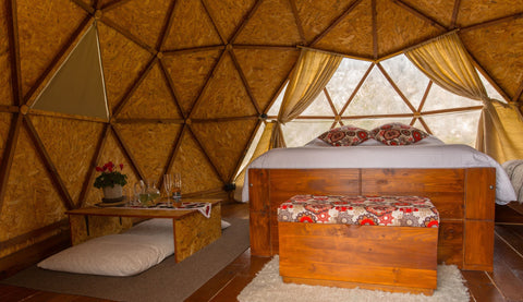 Interior del domo, configuración pareja cama doble, baul, mesa con flores naturales, copas con vino de gulupa de la casa y ventanal con vista a la montaña.